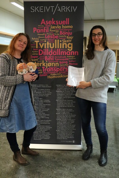 Hege Braathen and Dijana Stupar, two of those who initiated the auction bid, pose with the manuscript and to custom made doll versions of characters Isak and Even, also known under their couple name EVAK.