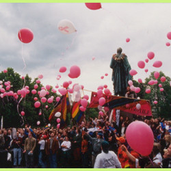 Queer parade, many people, several pink gas balloons in the air